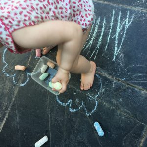 child drawing outside with floor chalks