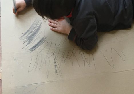 Holiday boredom is great for our children as it enables them to think creatively. Image is of a child drawing on cardboard.