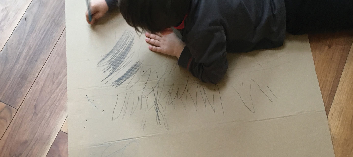 Holiday boredom is great for our children as it enables them to think creatively. Image is of a child drawing on cardboard.